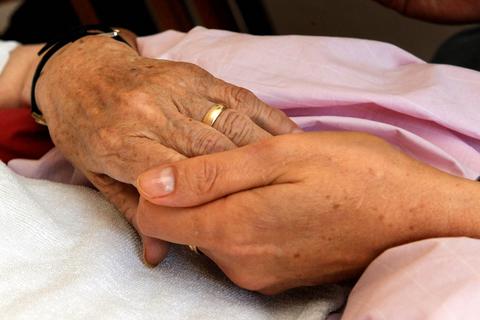 Eine Palliativhelferin hält die Hand eines todkranken Menschen.