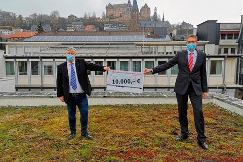 Der Sparkassenvorstandsvorsitzende Andreas Bartsch (rechts) übergibt Professor Martin Koch eine Spende für das "Breathing Project" - mit Sicherheitsabstand.  Foto: Sparkasse Marburg-Biedenkopf 