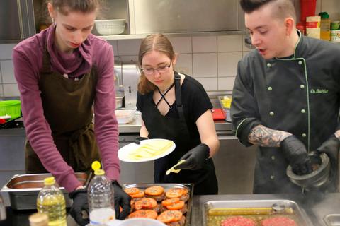 Kira Diez (von links), Tatjana Weidner und Koch Christopher Buttler bereiten die Burger für den Backofen vor.  Foto: Frank Rademacher 