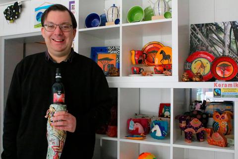 Pfarrer Christian Fahl mit einer Flasche Rotwein, die in einer genähten Tüte steckt, die es im Weltladen zu kaufen gibt. Foto: Frank Rademacher 