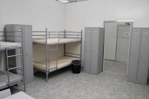 Blick in ein noch unbelegtes Zimmer einer Flüchtlingsunterkunft: vier Doppelstockbetten, vier Schrankspinde, Tisch, vier Stühle.