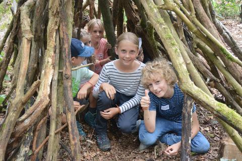 Die Kinder bauen sich im Wald ein Tipi aus Holzstöcken.