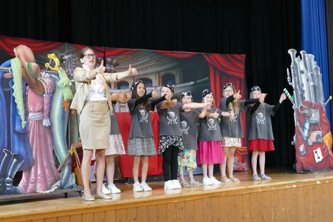 Raphaela Stürmer steht mit Oberbieler Grundschülern auf der Bühne: Der Verein „TourneeOper“ ist nach Oberbiel gekommen, um die Kinder spielerisch ans Thema Oper heranzuführen.