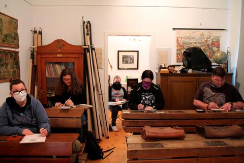 Sie sitzen auf den Schulbänken von 1920 und skizzieren ihre Umgebung: Die "Urban Sketchers" Mittelhessen arbeiten im Steindorfer Heimatmuseum. Foto: Markus Fritsch 