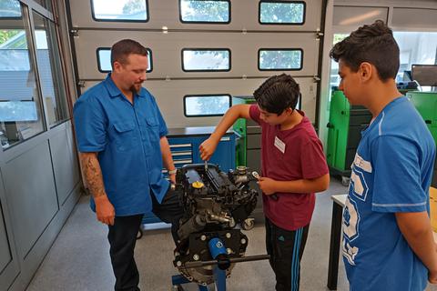 Ausbilder Niko Tursky (l.) erklärt Muhammed Ebert (M.), wie man beginnt, einen Motor aufzuschrauben.