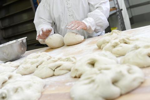 Ein Bäcker knetet Brötchen. 