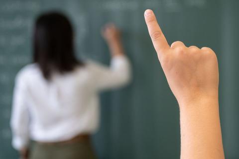 Ein Schüler meldet sich, während die Lehrerin an die Tafel schreibt.