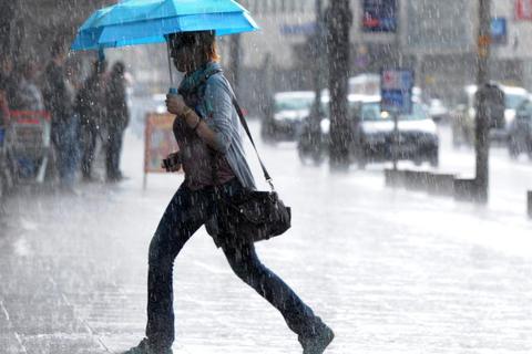 Eine Frau läuft mit einem Schirm durch den Regen. Symbolfoto: dpa 
