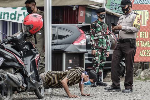 Indonesien, Makassar: Ein Motorradfahrer hat die Corona-Regeln missachtet und muss nun vor Polizisten Liegestütze machen. Foto: dpa