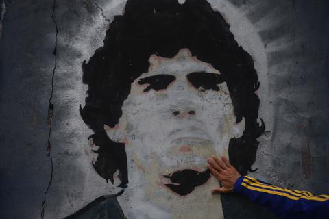 25.11.2020, Argentinien, Buenos Aires: Ein Fan des Fußballclubs Boca Juniors legt die Hand auf ein Wandgemälde mit der Abbildung des Fußballstars Diego Maradona am Tag seines Todes. Medienberichten zufolge starb Maradona in seinem Haus in Tigre nördlich von Buenos Aires an einem Herzinfarkt. Foto: Fernando Gens/dpa +++ dpa-Bildfunk +++