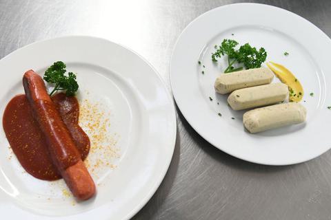 Eine vegane Currywurst und vegane Weißwürste liegen auf Tellern an der Essensausgabe im Hofbräuzelt auf dem Oktoberfest. © Felix Hörhager/dpa