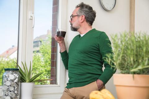 Ein Mann steht mit einer Tassee Kaffee am Fenster.