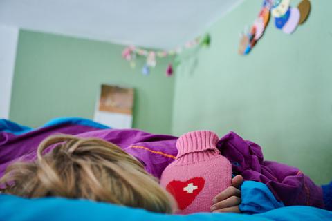 Ein Kind liegt mit Wärmflasche im Bett