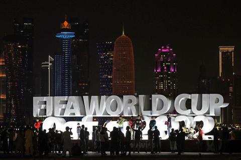 Menschen stehen vor der Eröffnung der WM vor einem beleuchteten Schriftzug „Fifa World Cup Qatar 2022“.