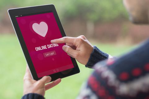 Ein junger Mann benutzt sein Tablet vor grünem Naturhintergrund, mit Online-Dating-App auf dem Bildschirm