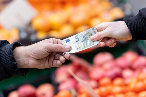 Ein Kunde bezahlt seinen Einkauf an einem Stand auf einem Wochenmarkt mit einem Fünf-Euro-Schein.